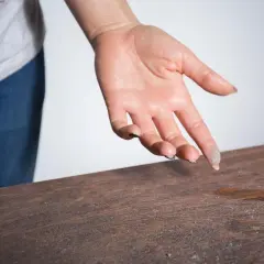 Mano con polvo en los dedos sobre una mesa de madera. Una demostración visual de cómo eliminar el polvo del aire y las superficies.