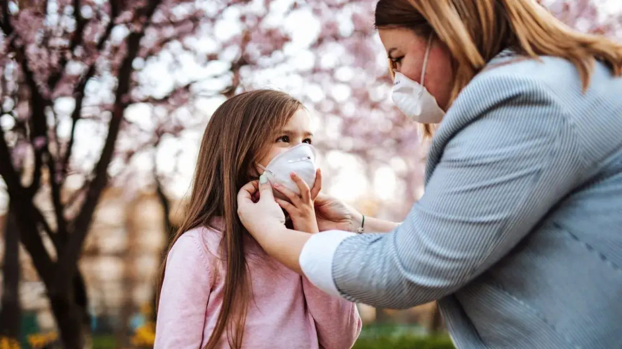 Madre ajusta mascarilla FFP2 a su hija bajo un árbol en flor. Una mascarilla FFP2 para que sirve, protege eficazmente.