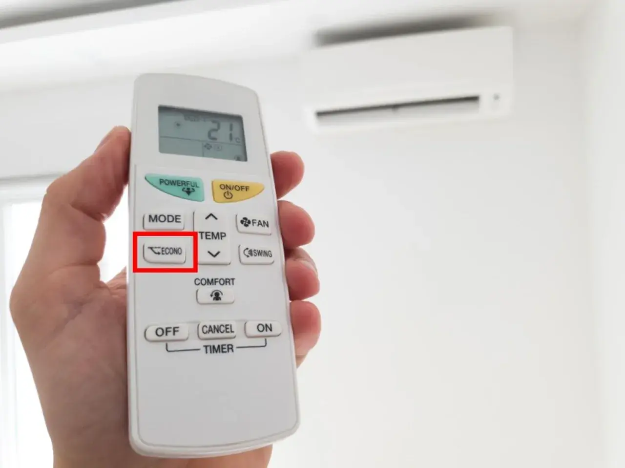 Mano sosteniendo un control remoto de aire acondicionado, con el botón "ECONO" resaltado. Activa el modo eco para ahorrar energía.