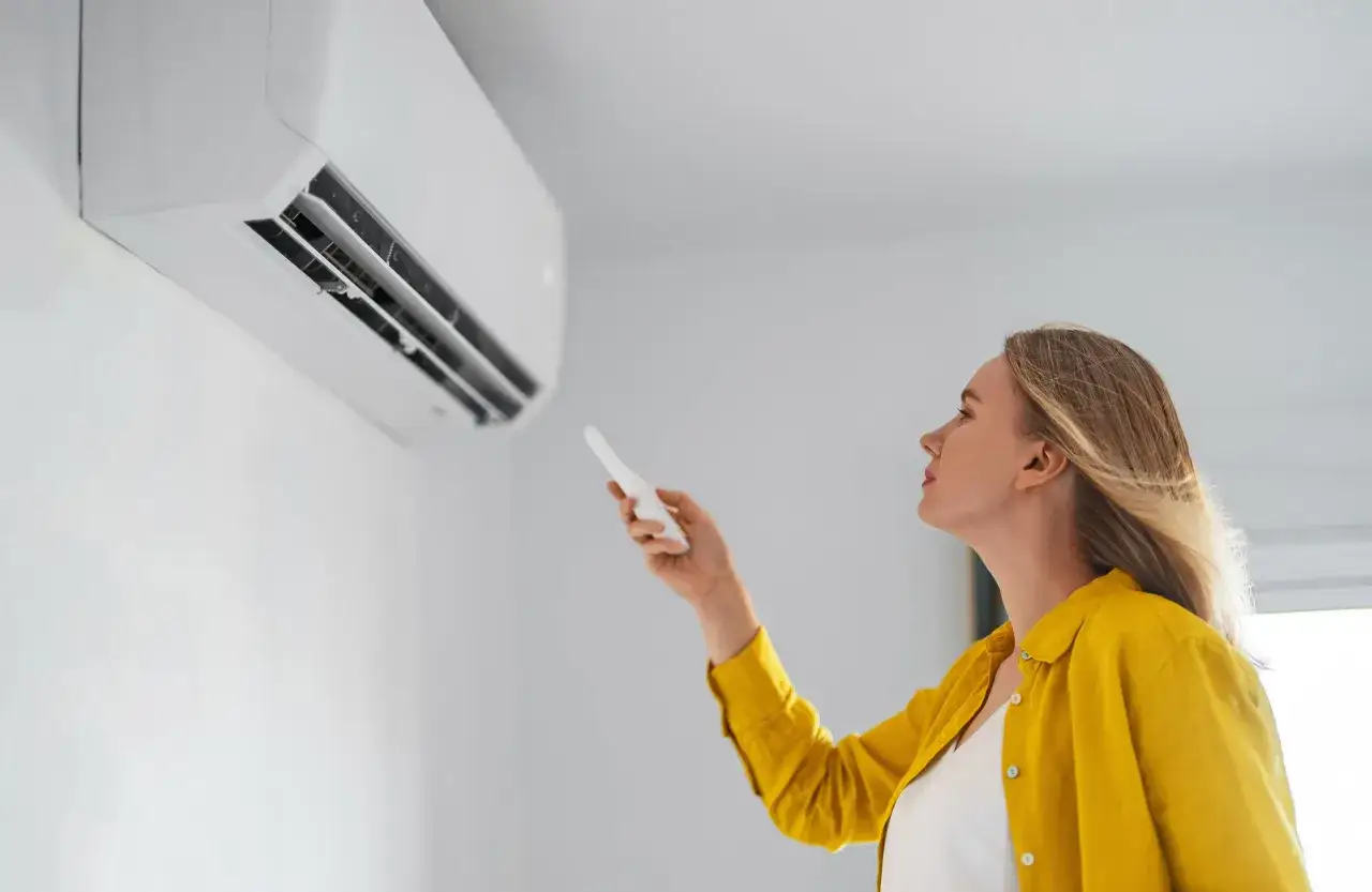 Mujer ajusta el aire acondicionado a la temperatura ideal para ahorrar energ&iacute;a.