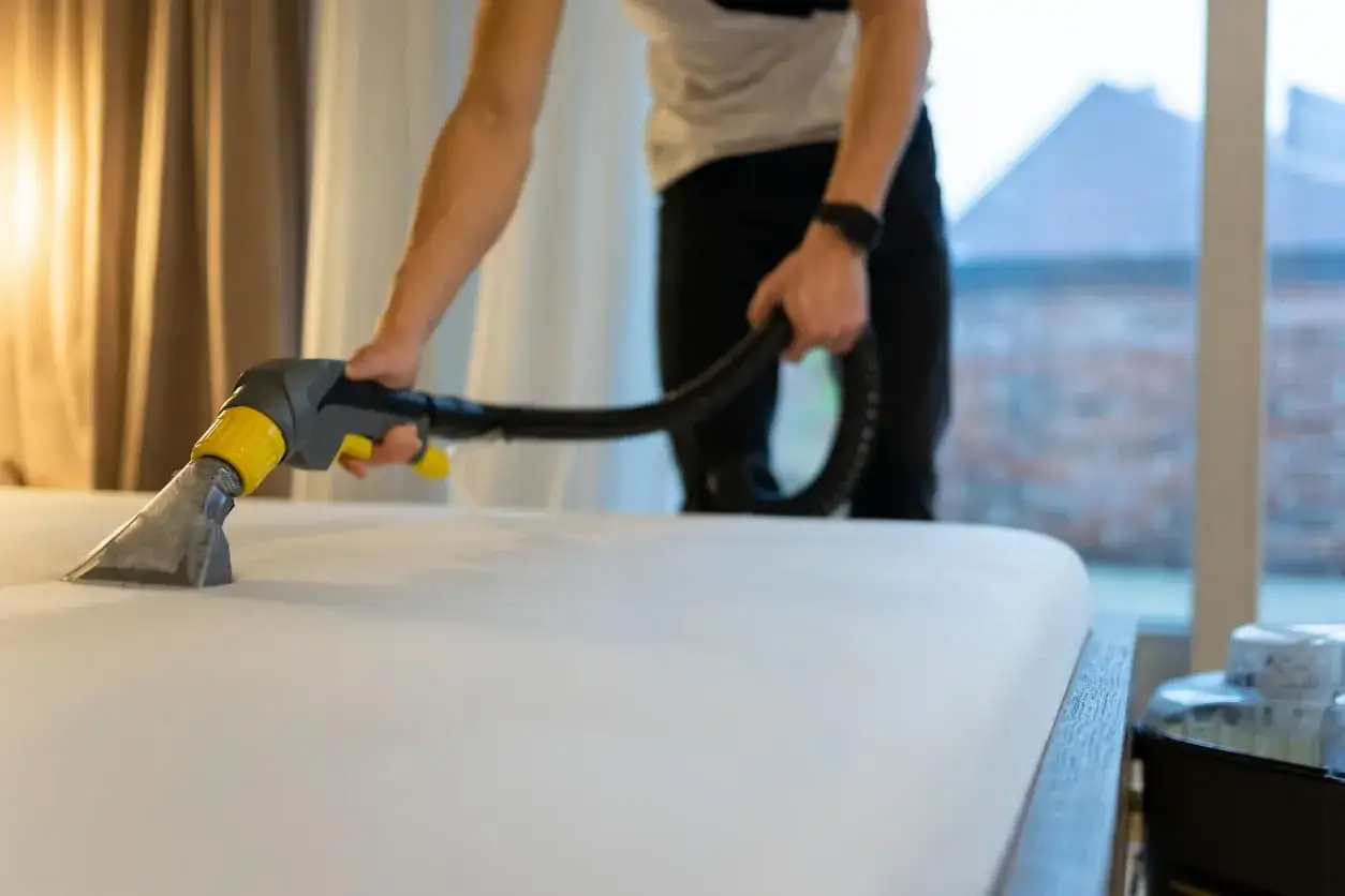 Persona usando un limpiador de tapicería para limpiar un colchón. Aprende cómo limpiar colchones en casa para un descanso más saludable.