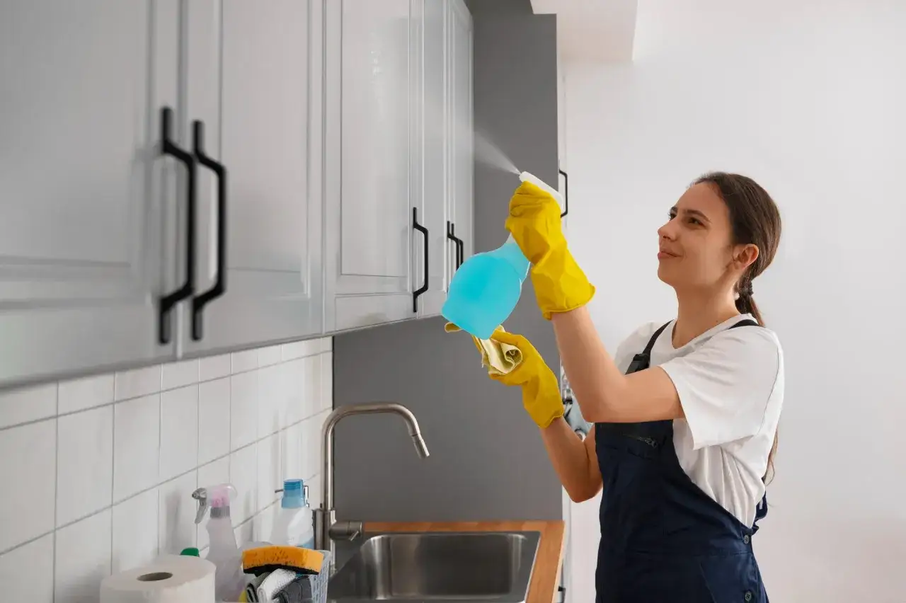 Mujer con guantes amarillos rocía desinfectante en los gabinetes de la cocina, un paso clave para saber como hacer que huela bien la casa.